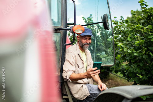 Male farmer using smartphone next to tractor in field