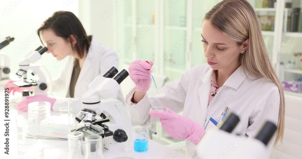 Two female scientists working in a laboratory and dripping blue liquid Two female scientists working in a laboratory and dripping blue liquid
