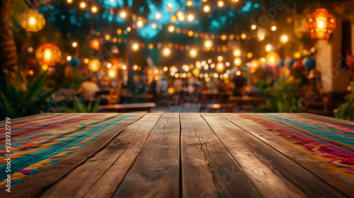 Empty wooden table set against a colorful Mexican blanket and lanterns hanging at a nighttime Cinco de Mayo festival