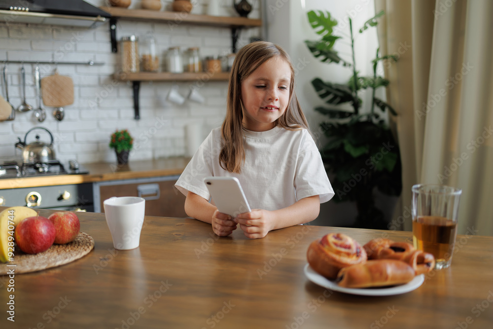 Positive kid holding cellphone near breakfast at home Positive kid holding cellphone near breakfast at home
