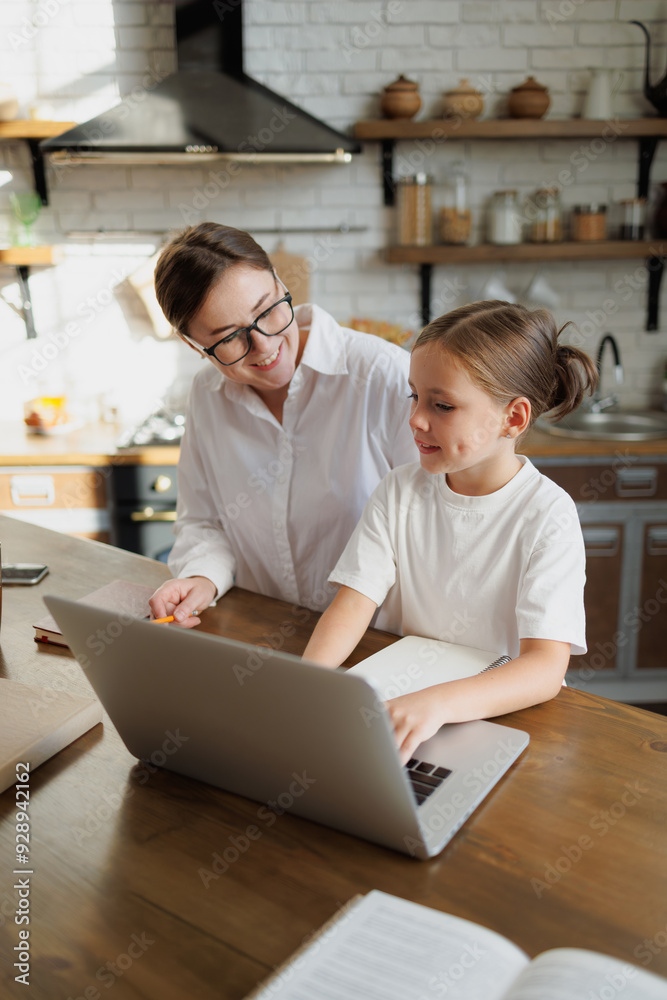 Smiling mother and kid using laptop during online education in kitchen Smiling mother and kid using laptop during online education in kitchen