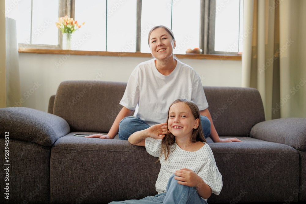 Smiling child looking at camera near mother on sofa at home Smiling child looking at camera near mother on sofa at home