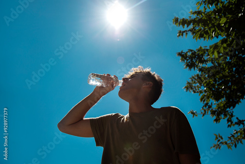 Young handsome man drinking water in hot sunny day. Surviving the heat concept