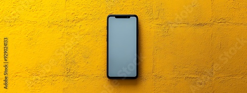  A modern smartphone with a sleek black frame and a blank white screen is displayed against a vibrant yellow background. The phone is centered and viewed from above, emphasizing its minimalist design 