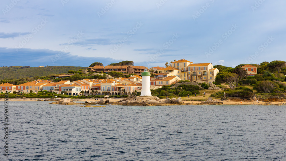 El faro de entrada al puerto de Palau, en Cerdeña, Italia, se alza sobre rocas que bordean la costa, rodeado de encantadoras casas de tonos pastel y techos de tejas rojas. El faro de entrada al puerto de Palau, en Cerdeña, Italia, se alza sobre rocas que bordean la costa, rodeado de encantadoras casas de tonos pastel y techos de tejas rojas.