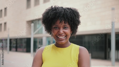 Close up individual portrait of one teenage african american girl smiling and looking at camera outside. A young adult woman staring front and laughing. Afro female gazing with friendly expression