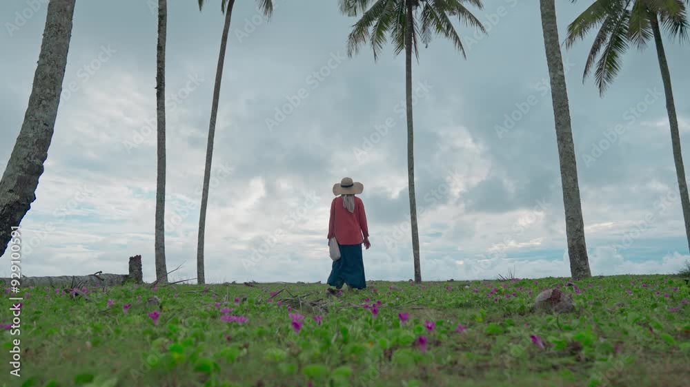 A woman walks through coconut trees towards the beach A woman walks through coconut trees towards the beach