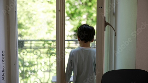 Young boy reaching for the window knob, stepping out onto the balcony to explore, and returning home to close the window. curiosity and interaction with the outdoor environment