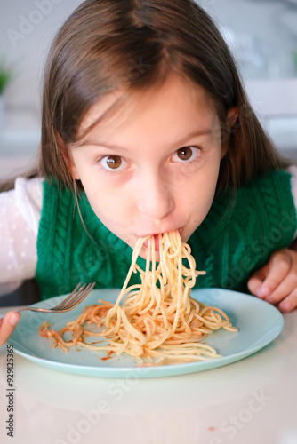 Portrait of girl having fun eating spaghetti. Child twists pasta on fork. Baby food concept. Vertical image.