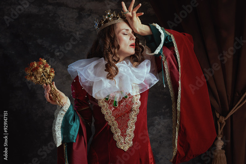 disappointed medieval queen in red dress with dried flower