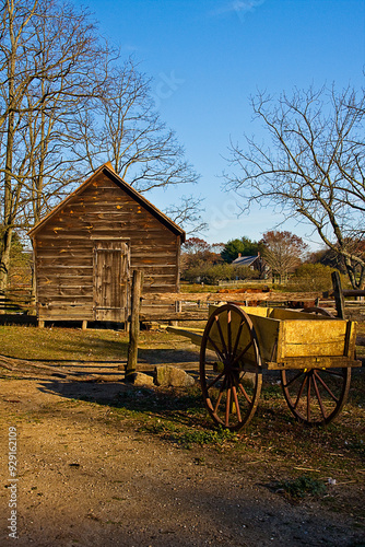 Old wooden shack on farm in autumn, with rustic wagon in foreground.