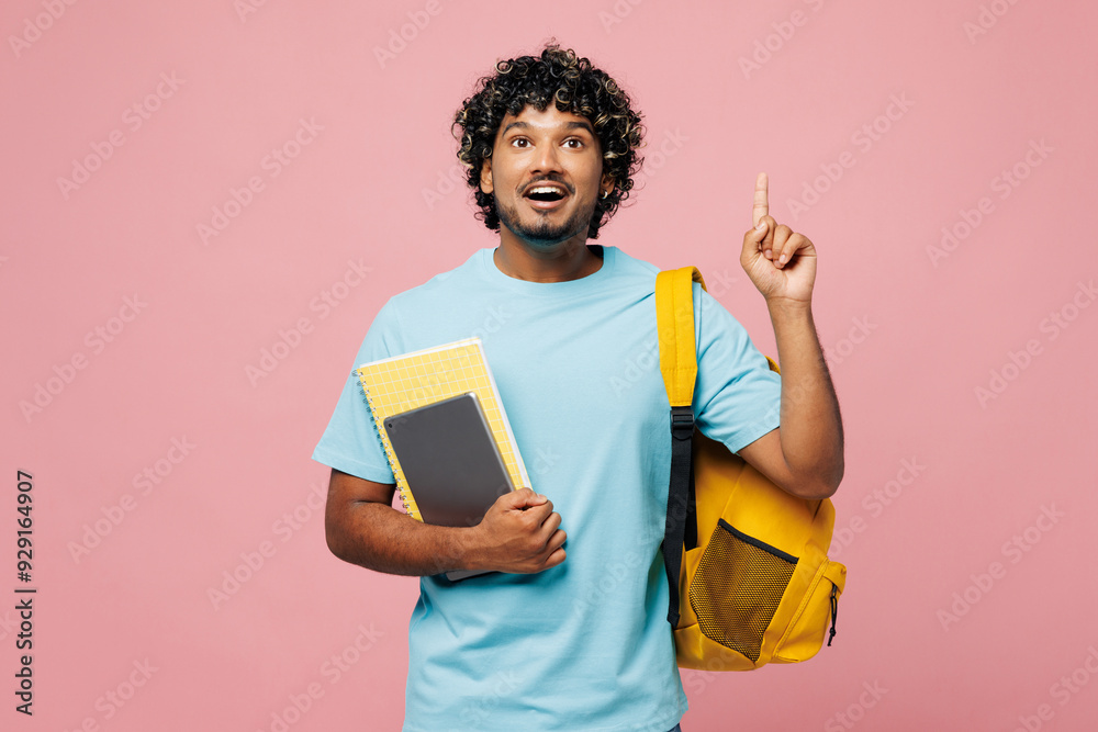 Young Indian boy student wear blue t-shirt casual clothes backpack bag hold books point index finger overhead on blank area isolated on plain pink background. High school university college concept. Young Indian boy student wear blue t-shirt casual clothes backpack bag hold books point index finger overhead on blank area isolated on plain pink background. High school university college concept.