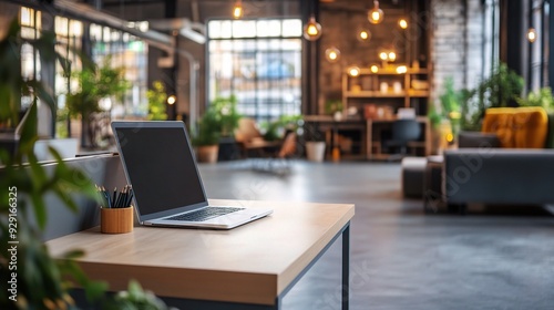 Modern Loft Office Workspace: A sleek laptop sits open on a wooden desk in a spacious, modern loft office, bathed in warm lighting and surrounded by lush greenery