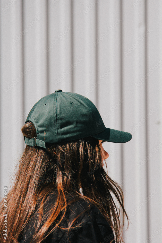 A profile view of a woman wearing a green cap. The light, subtle blur, and graininess focus attention on her relaxed posture, creating a minimalist yet visually compelling image.