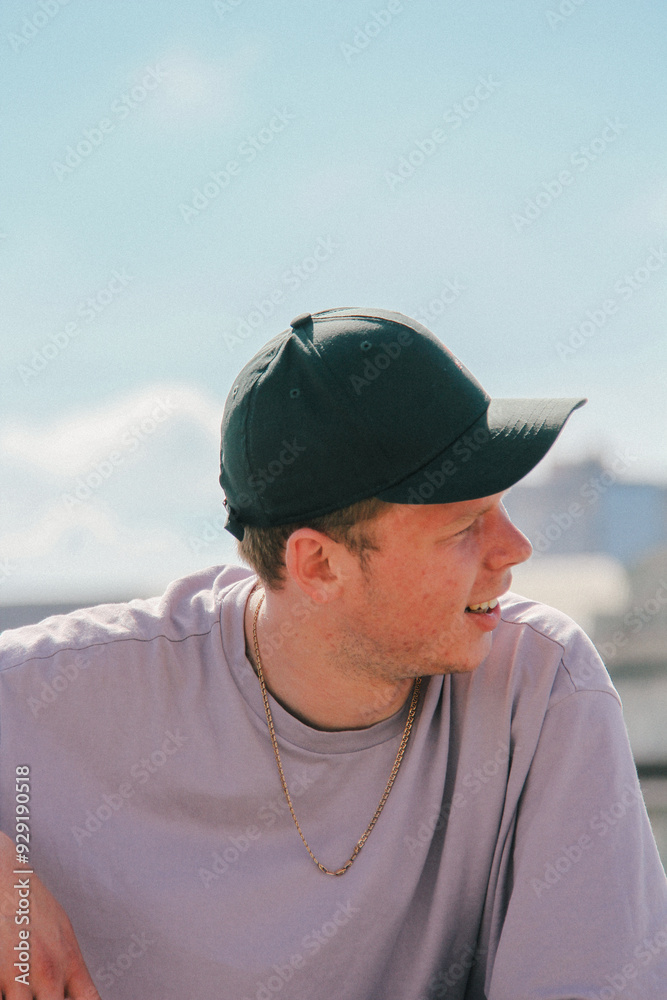 A young man in a green cap gazes off into the distance with a thoughtful expression. The slight blur and natural grain add an artistic dimension to the portrait.