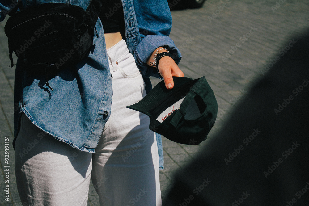 A close-up shot of a woman holding a green cap, her denim jacket and accessories contributing to a casual style. The lighting, focus, and graininess create a warm, artistic composition.