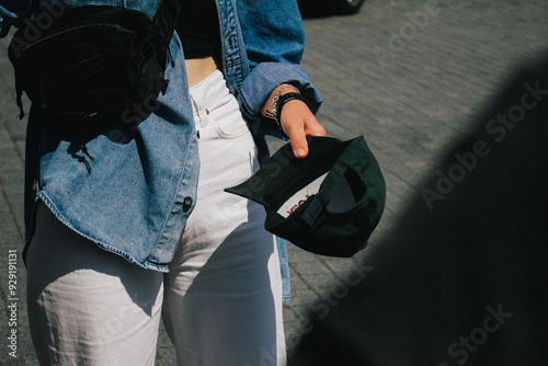 Obraz na płótnie A close-up shot of a woman holding a green cap, her denim jacket and accessories contributing to a casual style. The lighting, focus, and graininess create a warm, artistic composition. w salonie