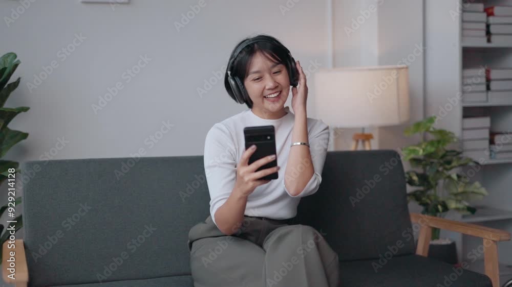 Young woman sitting on a sofa, wearing headphones, enjoying music on her smartphone, radiating happiness and relaxation Young woman sitting on a sofa, wearing headphones, enjoying music on her smartphone, radiating happiness and relaxation
