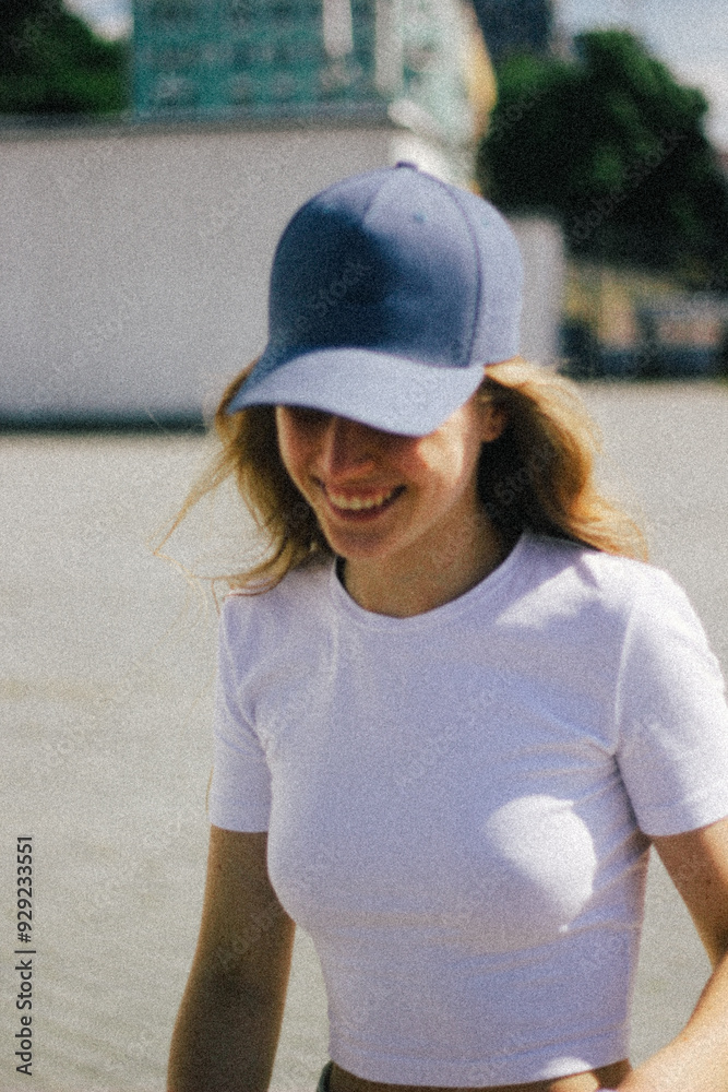 Back view of a young woman with long blonde hair, wearing a blue cap, looking out into the distance. The focus on her hair and the cap in natural light creates a serene, contemplative mood.