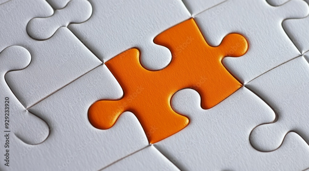 Fototapeta premium A bright orange puzzle piece stands out among white jigsaw pieces, symbolizing uniqueness and individuality