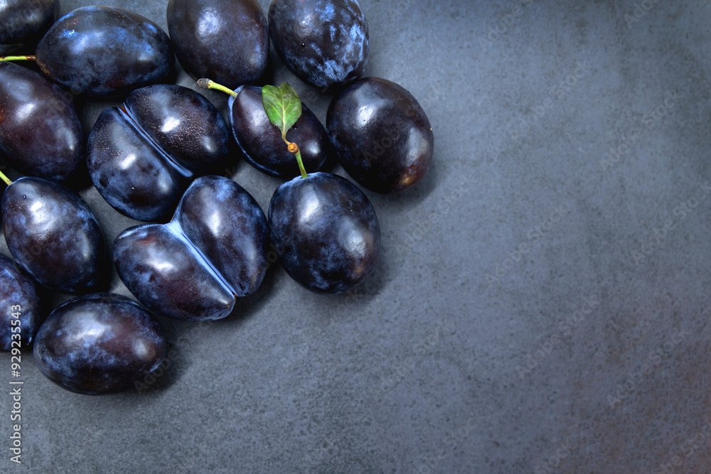 Fresh ripe plums on a dark slate background. A cluster of fresh ripe plums is displayed on a dark slate background, with one plum featuring a small green leaf. Top view. Copy space.