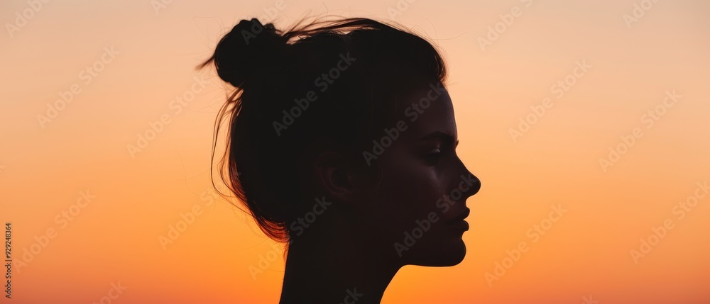 A woman's silhouette, hair in a bun, against an orange-yellow sky Sun resides in background A woman's silhouette, hair in a bun, against an orange-yellow sky Sun resides in background