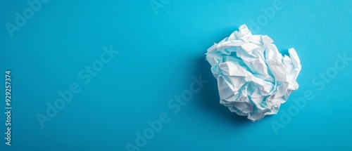  A crumpled paper rests atop a blue surface, near a ball of white paper also placed there Both items reside on the blue surface