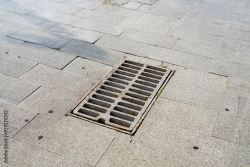 A round manhole cover is resting on the surface of a brick sidewalk, creating an interesting visual contrast with its surroundings, which include the patterned bricks all around it