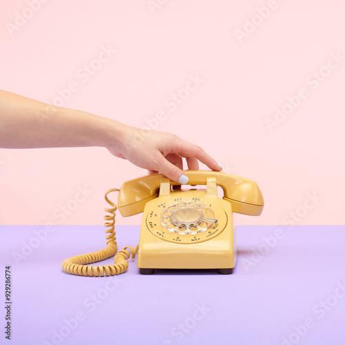 Yellow Retro Vintage Rotary Phone on Purple and Pink Tablet Top Set Still Life with Hand Reaching and Holding photo