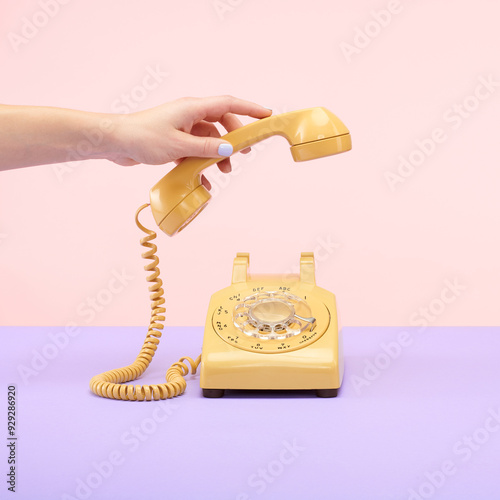 Yellow Retro Vintage Rotary Phone on Purple and Pink Tablet Top Set Still Life with Hand Reaching and Holding photo