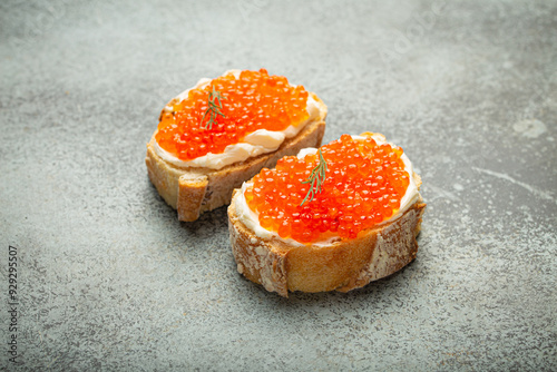 Photography Two caviar toasts baguette canape with butter and red salmon caviar top view on grey concrete background, festive luxury delicacy and appetizer