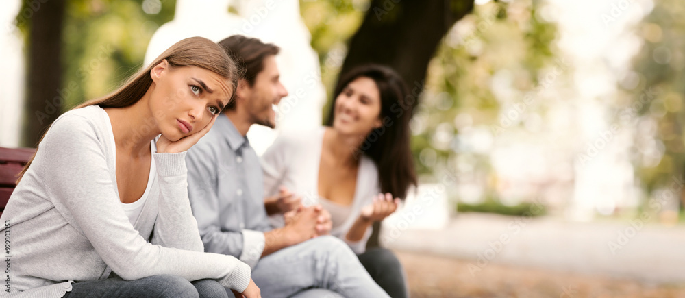 Depressed Girl Sitting Next To Happy Friends And Suffering From Loneliness In Park Outside. Selective Focus Depressed Girl Sitting Next To Happy Friends And Suffering From Loneliness In Park Outside. Selective Focus