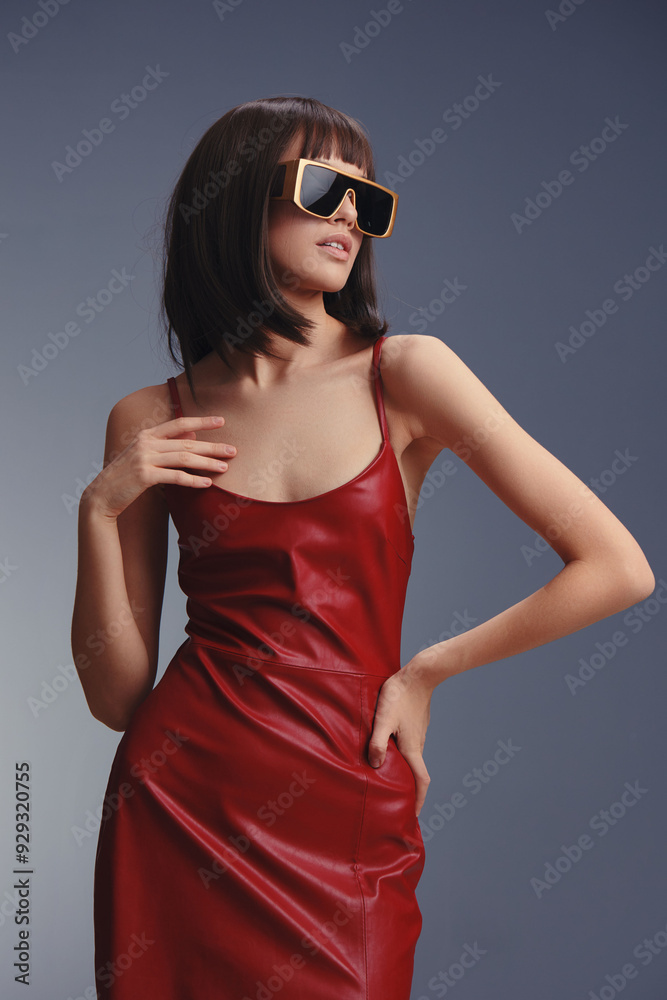Red leather dress and sunglasses a woman confidently poses with her hands on her hips, wearing a stylish red leather dress and sunglasses, against a gray background Red leather dress and sunglasses a woman confidently poses with her hands on her hips, wearing a stylish red leather dress and sunglasses, against a gray background