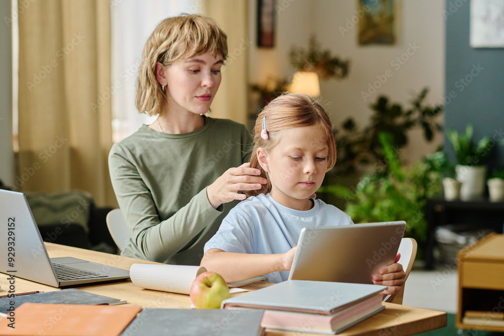 Young mother doing hair for her kid while she watching cartoon via tablet Young mother doing hair for her kid while she watching cartoon via tablet