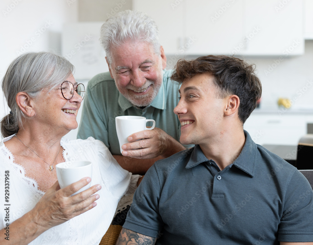 Happy multigenerational family sitting relaxing on sofa, grandparents drink a coffee cup while young grandson uses laptop. Positive emotions Happy multigenerational family sitting relaxing on sofa, grandparents drink a coffee cup while young grandson uses laptop. Positive emotions