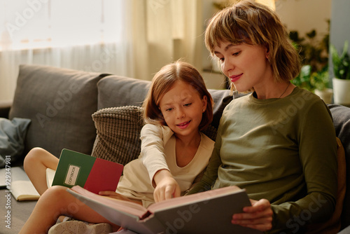 Little girl sitting next to her mom and reading book together