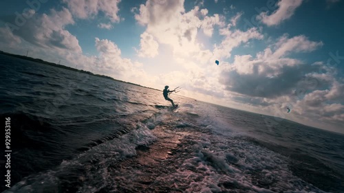 Kite surfer against beautiful cloudy sunset at sea. Slow motion of professional male kiteboarder moving fast on waves downwind