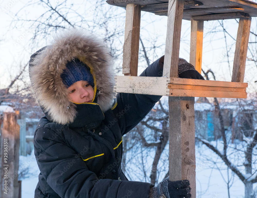Adorable child, boy feeding birds on a cold winter day, pouring grain into a feeder. A child helps birds in winter. Winter activities for children.