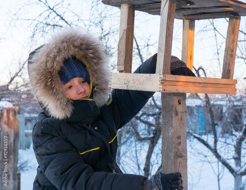 Obraz na płótnie Adorable child, boy feeding birds on a cold winter day, pouring grain into a feeder. A child helps birds in winter. Winter activities for children. w salonie