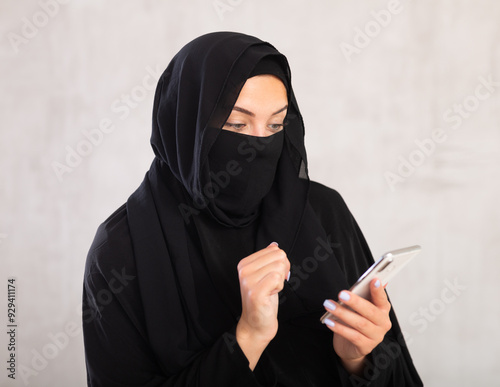 Tableau sur toile young light-skinned girl with her face covered by burka holds phone and types te
