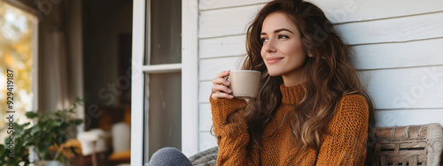 A young Caucasian woman wearing a cozy brown sweater is enjoying a warm beverage on a porch, exuding a relaxed and peaceful mood. photo