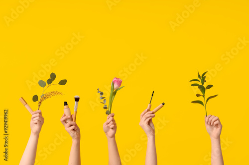 Female hands with tulip, concealer, foundation, brush, mascara and branches on yellow background