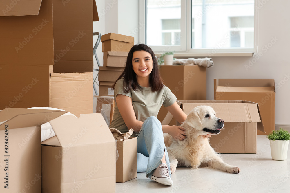Fototapeta premium Young happy woman and cute Labrador dog with boxes on moving day sitting at home