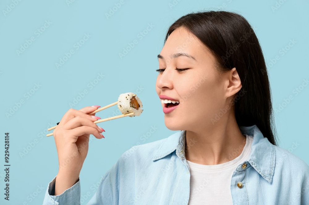 Beautiful young Asian woman eating tasty sushi roll with chopsticks on pale blue background, closeup Beautiful young Asian woman eating tasty sushi roll with chopsticks on pale blue background, closeup