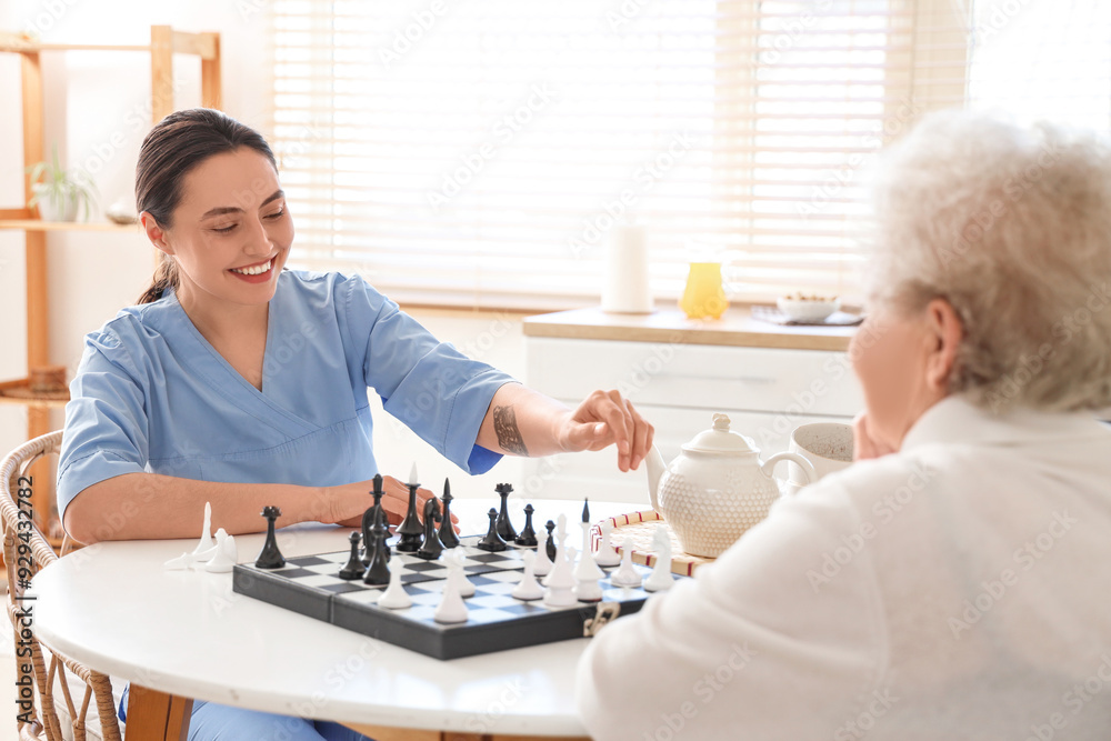 Physical therapist with senior woman playing chess at table in kitchen Physical therapist with senior woman playing chess at table in kitchen