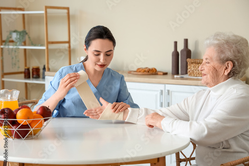 Physical therapist bandaging senior woman's arm in kitchen