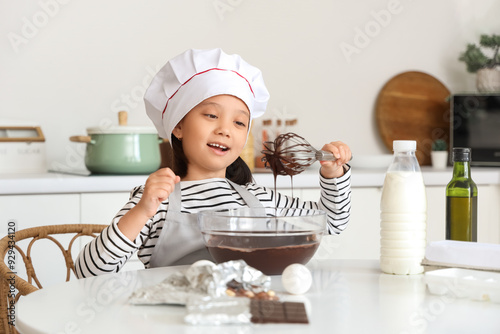 Funny little Asian girl whisking melted chocolate in kitchen photo