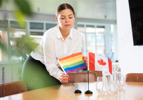 Assistant girl prepares office for international negotiations and meetings of leaders. Lady sets miniatures flags of Canada and LGBT on table. Close-up photo