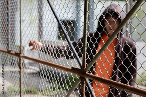 Fotografía Asian male teenager puts his hand on the metal fence around detention center of his village because he was detained for inappropriate behavior, freedom and detention of young people concept