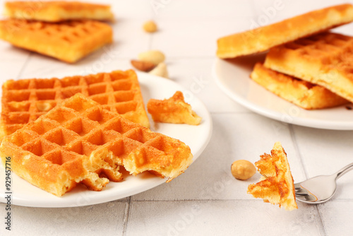 Plates with tasty Belgian waffles and different nuts on white tile background